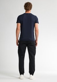 Námořnické bavlněné tričko s kulatým výstřihem, v kombinaci s černými cargo kalhotami se bočními kapsami a elastickými manžetami. Bílí tenisky dotváří celý outfit.