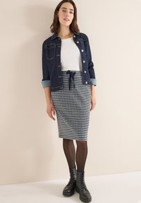 Denim jacket met knoopsluiting, witte crew-neck t-shirt, en knielange houndstooth rok met trekkoord. Zwarte veterschoenen en panty's.