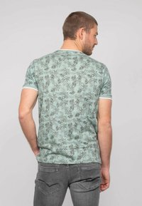 T-shirt vert menthe à manches courtes avec un motif de feuilles noir, doté d'un col et de poignets blancs contrastants, porté avec un jean gris.