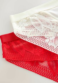 Weiße und rote Spitzenunterwäsche mit Blumenmustern, die auf einer hellen Oberfläche geschichtet ist.