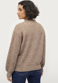 Maglione beige lavorato a maglia con una vestibilità ampia, texture a coste e maniche larghe. L'orlo è leggermente più lungo sul retro, creando una silhouette informale.