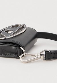 Juodos odos raktų dėklas su sidabriniu metaliniu logotipu ir sidabrine segtimi, pritvirtinti prie priderintos juodos juostos ant balto fono.