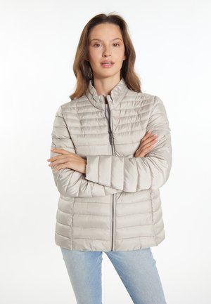 Lichtbeige pufferjack met een quiltpatroon, hoge kraag, volledige rits en lange mouwen. Gestyled met lichtblauwe jeans.