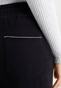 Sorte bomuldsbukser med en tekstureret talje og en baglomme udformet med hvid syning. Slim fit design, ingen synlige udsmykninger.