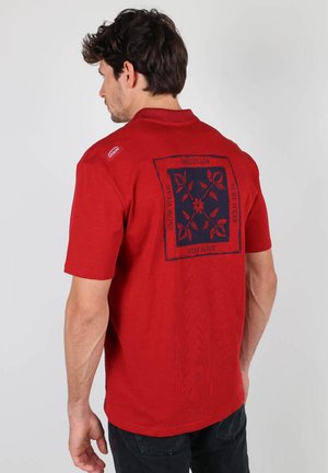 Polo rouge à manches courtes avec un design à motifs navy au dos, comportant du texte et des accents floraux. En coton, coupe décontractée.