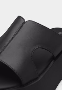 Μαύρο σανδάλι με λουρί από δέρμα που έχει ευρεία καμπυλωτή εγκοπή και ορατό ράψιμο σε μια ενιαία σόλα.