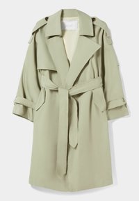 Světlý zelený trench coat vyrobený z hladké tkaniny, se širokým límcem, opaskem v pase a velkými předními kapsami. Otočené rukávy s knoflíkovými detaily.