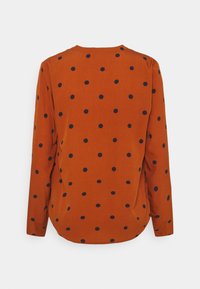 Chemise à manches longues en orange rouille avec des pois bleus, tissu doux, encolure ronde et ourlet incurvé à l'arrière.