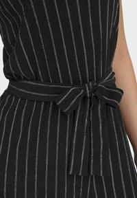 Vestido a rayas blanco y negro con una tela texturizada; presenta un cinturón atado en la cintura y finas rayas verticales para un contraste visual.