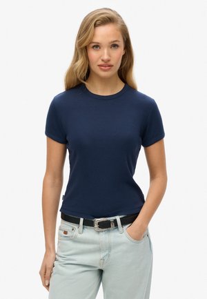 T-shirt bleu marine à manches courtes avec un col rond, texture côtelée et un petit logo de marque brodé sur la poitrine, associé à un jean bleu clair.