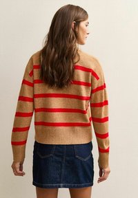 Maglione beige con strisce orizzontali rosse, realizzato in materiale morbido. Presenta un orlo a coste. Indossato sopra una mini gonna in denim scuro.