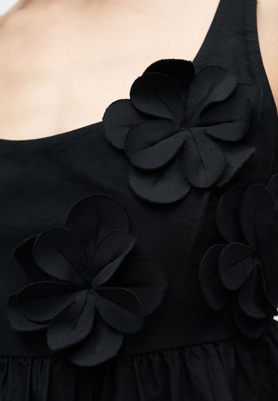Sort kjole med en innsvingt livdel og tredimensjonale stoffblomster i sort, med en teksturert, samlet nederdel.