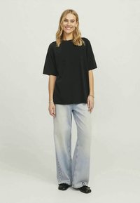 Svart oversized t-shirt med korta ärmar, matchad med ljusblå vida jeans. Modellen har på sig svarta slip-on-skor med en ren, enkel design.
