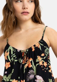 Camiseta floral en negro con flores naranjas y verdes, tirantes ajustables y un detalle de lazo en el escote. Tela ligera, de corte relajado.