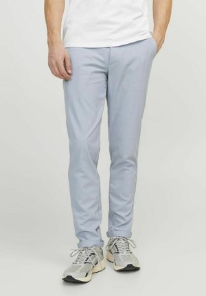 Pantalones azul claro de corte slim hechos de una tela texturizada, con bolsillos frontales y puños enrollados, combinados con zapatillas deportivas grises.