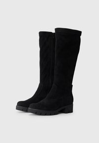 Schwarze Wildleder Stiefel bis zum Knie mit einer flachen, klobigen Gummisohle und seitlichem Reißverschluss. Sie haben eine abgerundete Zehenpartie und eine glatte Textur.