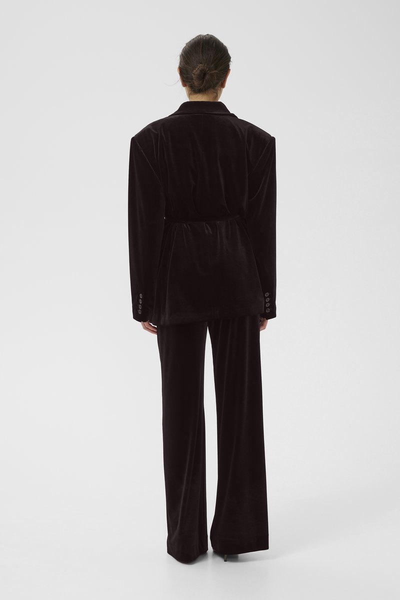 Schwarzer, taillierter Blazer aus Samt mit breiten Schultern, tailliertem Gürtel und passenden weit geschnittenen Hosen; glatte Textur mit subtiler Schattierung.