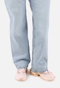 Zapatillas deportivas rosas con parte superior de malla texturizada, suela gruesa y de color claro, combinadas con jeans de mezclilla de un azul claro y un ajuste ligeramente holgado.