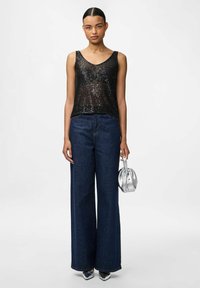 Top senza maniche nero con paillettes, pantaloni in denim a vita alta e a gamba larga, borsa argentata e tacchi metallici creano un look coeso.