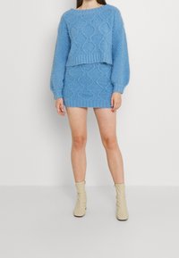 Ljusblå stickad tröja och minikjol i set med strukturerade diamantmönster; ribbade ärmslut och fåll; parat med beige ankelstövlar.