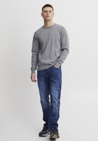 Grå genser med rund hals, kombinert med blå denimjeans og svarte joggesko. Glatt tekstur, klassisk passform og avslappet stil.
