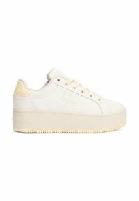 Baskets blanches et jaune pâle en cuir avec une semelle épaisse, dotées de lacets ronds, de détails de couture et d'un logo sur le côté.
