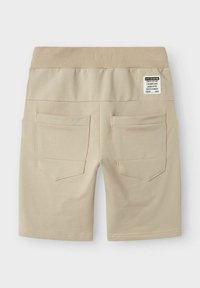 Shorts en coton beige avec une large taille élastique, comportant deux poches arrière et une étiquette d'entretien, texture lisse et design mi-genoux.
