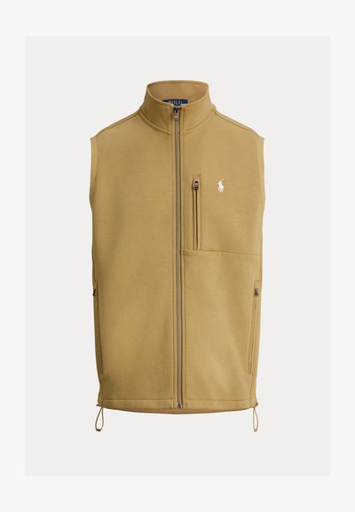 Bezrekawnik w kolorze khaki z wysokim kołnierzem, pełnym suwakiem z przodu, kieszenią na piersi po lewej stronie oraz kieszeniami bocznymi; posiada wyszywane logo na piersi.