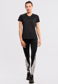 Maglietta atletica nera a maniche corte abbinata a leggings a fantasia con accenti blu chiaro, grigi e neri. Inclusi scarpe sportive nere.
