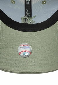 Baseballcap aus hellgrünem Material, mit schwarzem Schirm und einem runden MLB-Echtheitsaufkleber, der ein Baseballdesign zeigt.