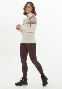 Pull en maille crème avec une encolure ornée de motifs roses et bleus ; associé à un legging moulant bordeaux avec des accents gris et des zips. Bottes de randonnée noires.