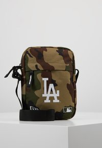 Borsa a tracolla camouflage realizzata in tessuto durevole. Caratterizzata da un logo LA bianco, una tracolla regolabile e una chiusura superiore con zip. Forma quadrata.