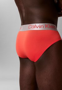 Calvin Klein Herren-Slips in lebhaftem Korallrot, mit einer weichen, glatten Textur und einem kontrastierenden grauen elastischen Bund mit Markenlogo.