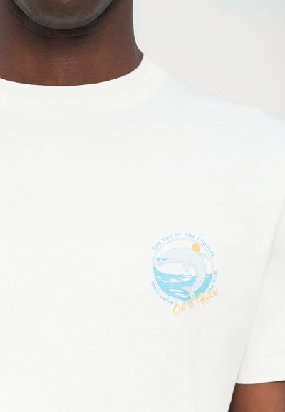 Hvid bomulds t-shirt med et rundt grafisk motiv i blå og orange, der forestiller en delfin med teksten "Vi ses på den anden side, ude af kontoret."