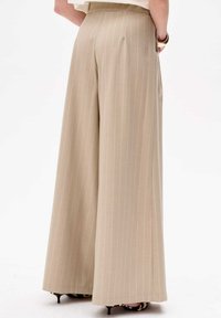 Beige, hooggetailleerde broek met wijde pijpen en subtiele verticale streepjes. Kenmerkt zich door een zachte textuur en geplooide details aan de achterkant.