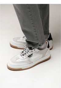 White and gray sneaker with suede and leather panels, black accents, lace-up closure, and a textured gum rubber sole. Designed for casual wear.