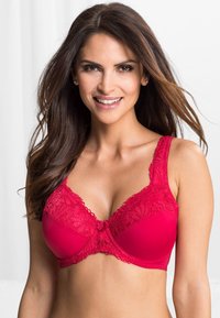 Soutien-gorge rouge en tissu lisse, avec des détails en dentelle florale sur les bonnets et les bretelles, présentant un nœud décoratif au centre et un soutien sous la poitrine.