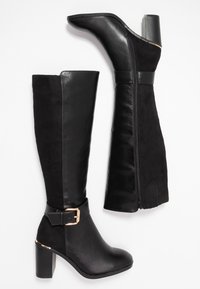 Black knee-high boots with a leather and suede exterior. Features a buckle accent and a zipper closure. Chunky high heel design.
