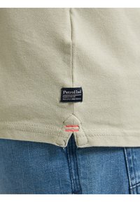Khaki katoenen shirt met een gestructureerde afwerking, voorzien van een logo patch en rode steekaccenten aan dezoom. Gepaard met blauwe spijkerbroek.