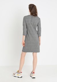 Grå rutiga klänning med trekvartslånga ärmar, åtsittande silhuett och dragkedja i ryggen, bärs med sportiga sneakers.