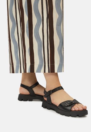 Črne usnjene sandale z nastavljivimi trakovi, robatimi gumijastimi podplati in okrasno sponko, v kombinaciji z nagubanimi krili z valovitimi črtami.
