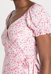 Růžové květinové šaty s vycpanými rukávy a výstřihem do V. Mají polorozpínací design a detail s uvázáním v pase. Měkká bavlněná látka.