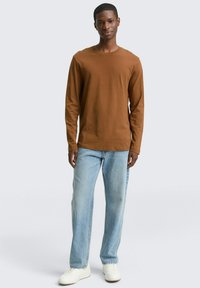 Lange mouw bruin shirt gecombineerd met lichtblauwe jeans en witte sneakers. Het shirt heeft een ronde halslijn en een gladde textuur.