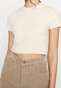 Krämfärgad kortärmad t-shirt i texturerad tyg, med rund halsringning, prydd med ljusbruna kordbyxor.