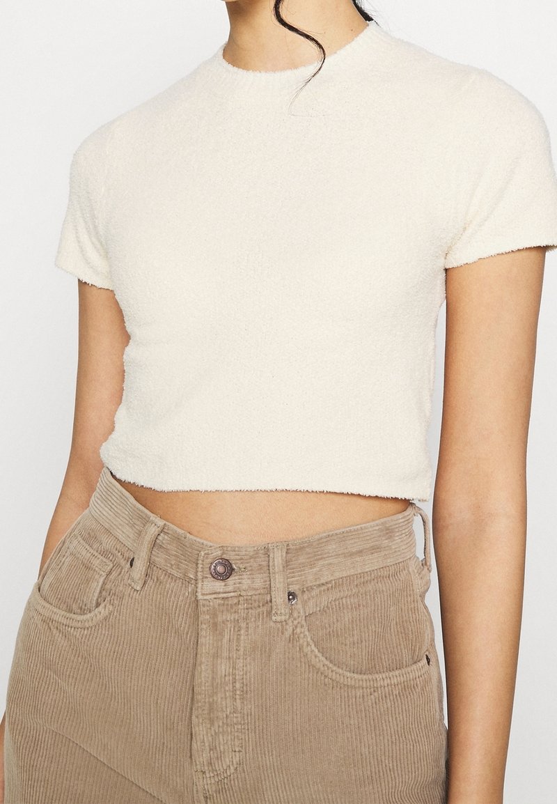 Krämfärgad kortärmad t-shirt i texturerad tyg, med rund halsringning, prydd med ljusbruna kordbyxor.