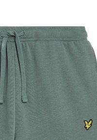 Pantaloni felpati verdi in cotone con vita elasticizzata, dettaglio con stringa e un piccolo logo giallo sulla gamba sinistra. Tessuto liscio.