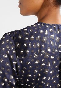 Blusa blu navy con motivo leopardato in marrone e bianco, dotata di scollatura rotonda e sottili maniche a sbuffo. Tessuto liscio.