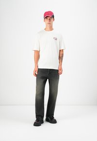 Hvid T-shirt med et lille burgunder grafisk motiv, sort og lyserød cap, grå denimbukser og sorte platformsko. Enkel, afslappet outfit.
