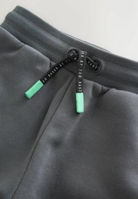 Grijze sportshorts met een gestructureerde stof, voorzien van een zwart trekkoord met groene uiteinden en merkdetails bij de tailleband.