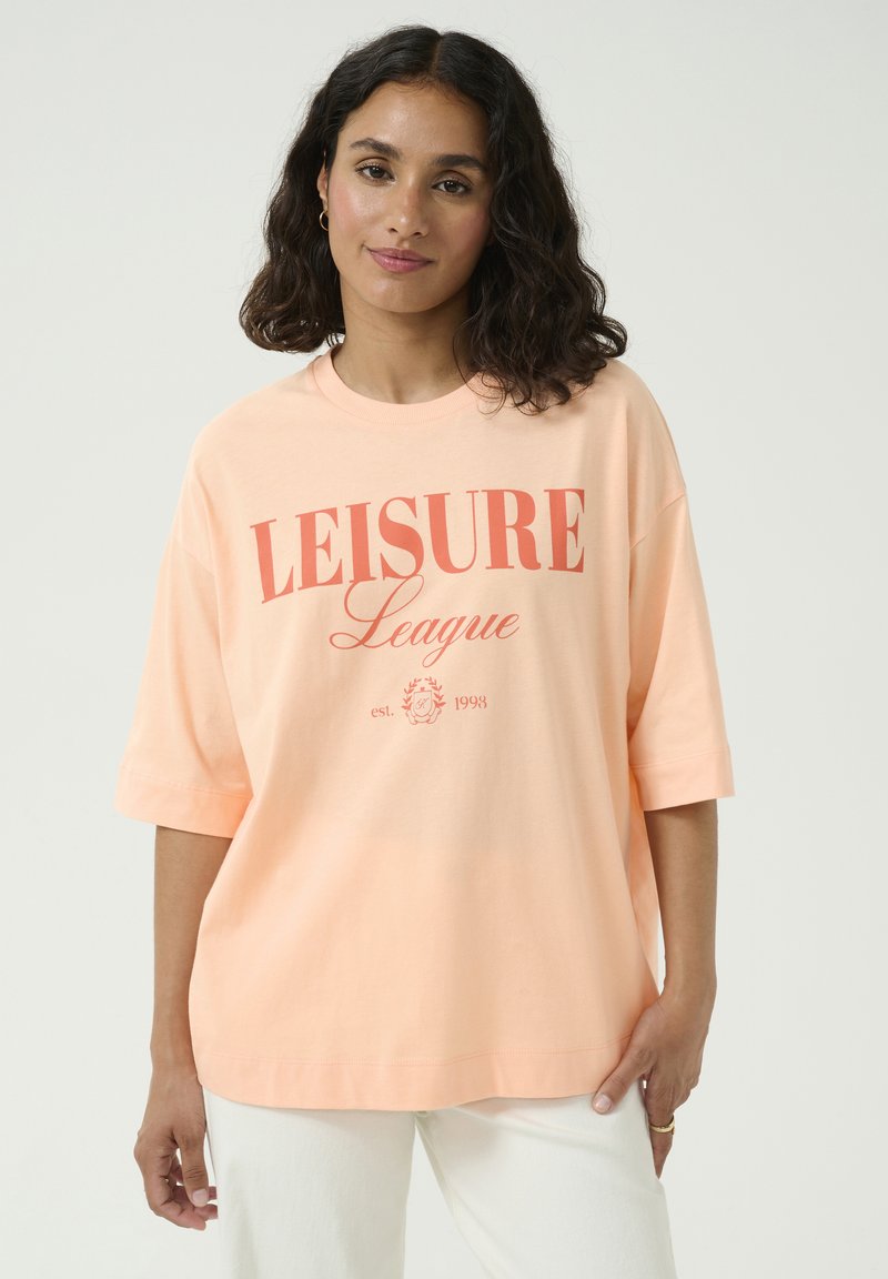 T-shirt surdimensionné couleur pêche, en coton, à manches courtes, avec le texte "LEISURE League" en corail et des détails floraux, coupe décontractée.